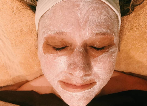 A woman relaxing with a facial mask applied to her face, eyes closed, at a spa offering comprehensive spa services.