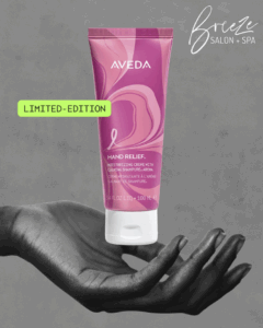 A tube of Aveda Hand Relief limited-edition moisturizer is displayed on an outstretched hand with "Breeze Salon + Spa" text in the background.